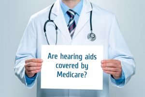 Doctor holds a sign asking if hearing aids are covered by Medicare. 