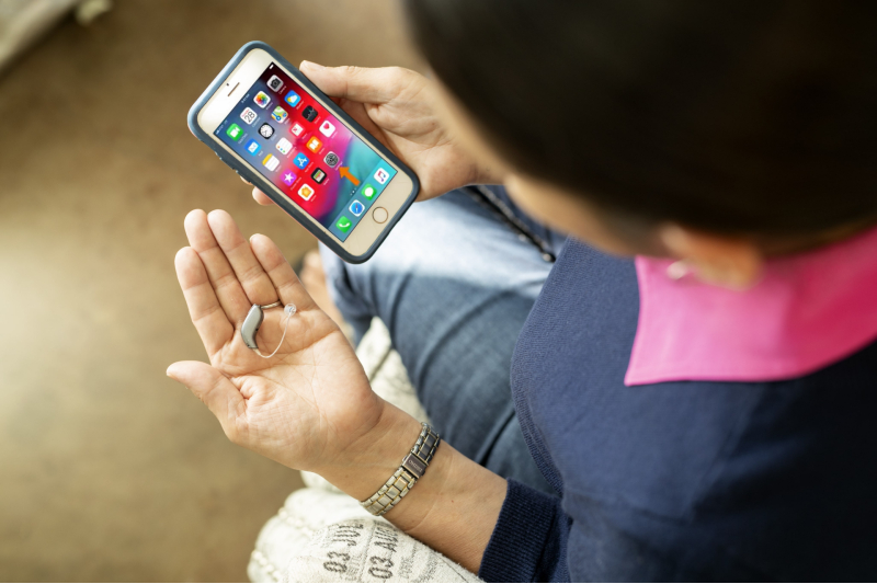 A woman holds her phone and hearing aids.