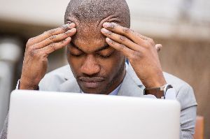 A man at a desk grabs his forehead from tinnitus and stress.